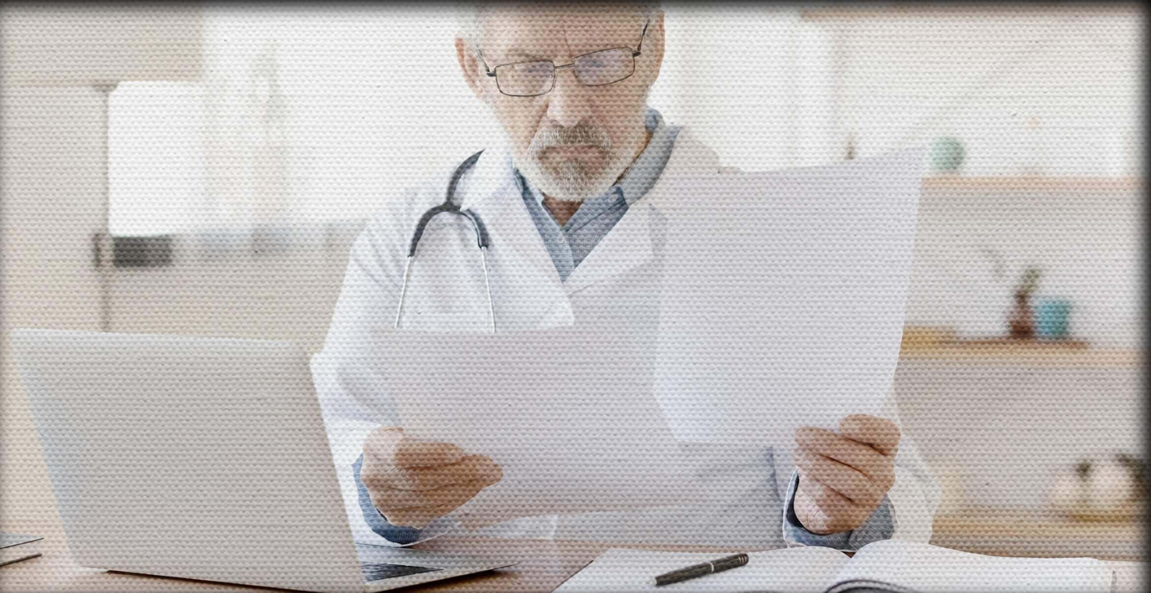 Doctor reviewing papers in front of a laptop